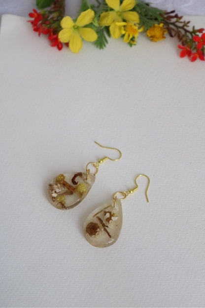 Teardrop-shaped earrings with floral design on a white background with flowers.