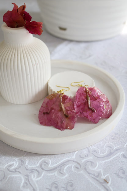 Pink earrings on a white dish with a white vase and red flower in the background.