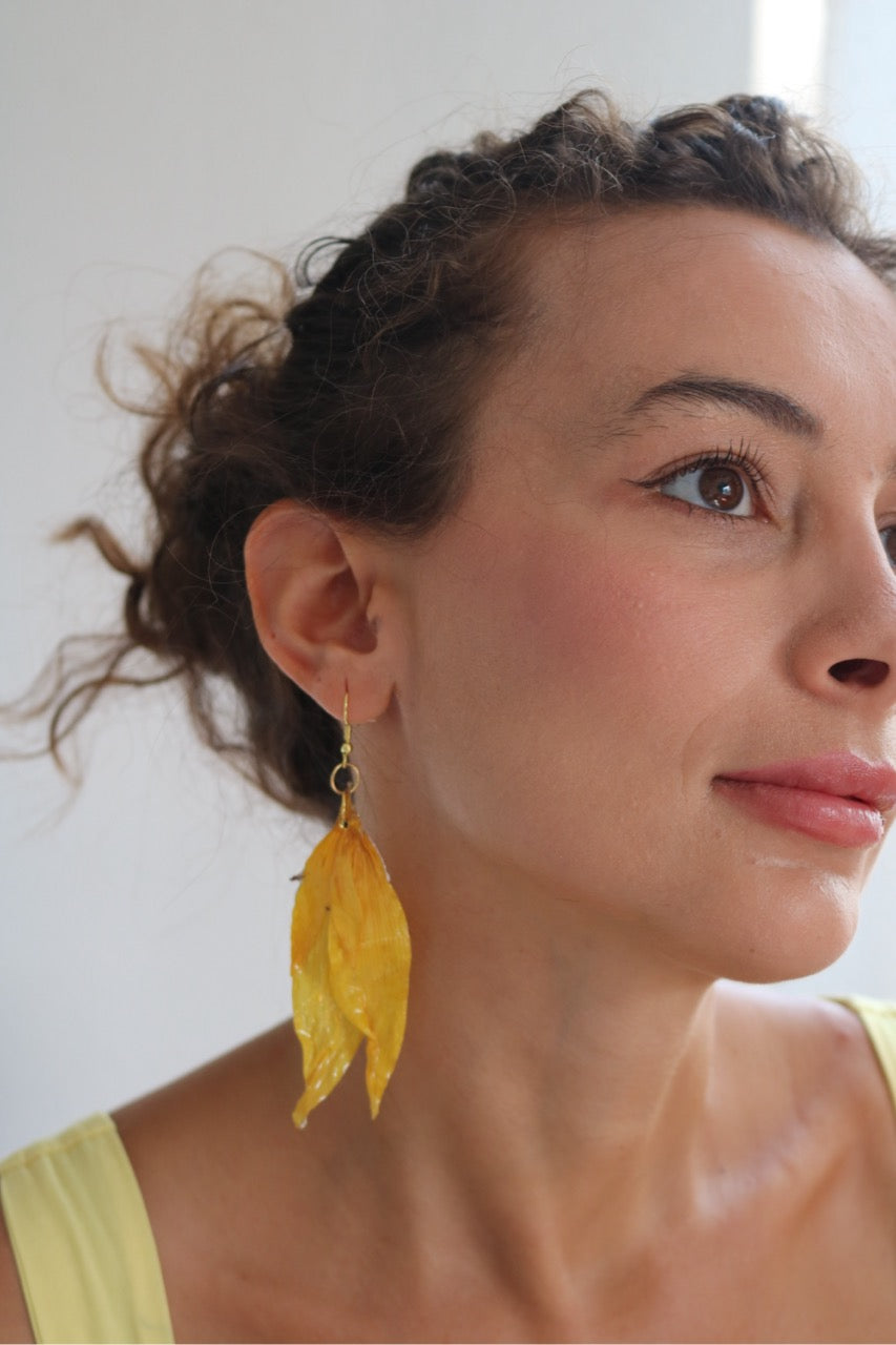 Woman wearing yellow leaf-shaped earrings against a white background