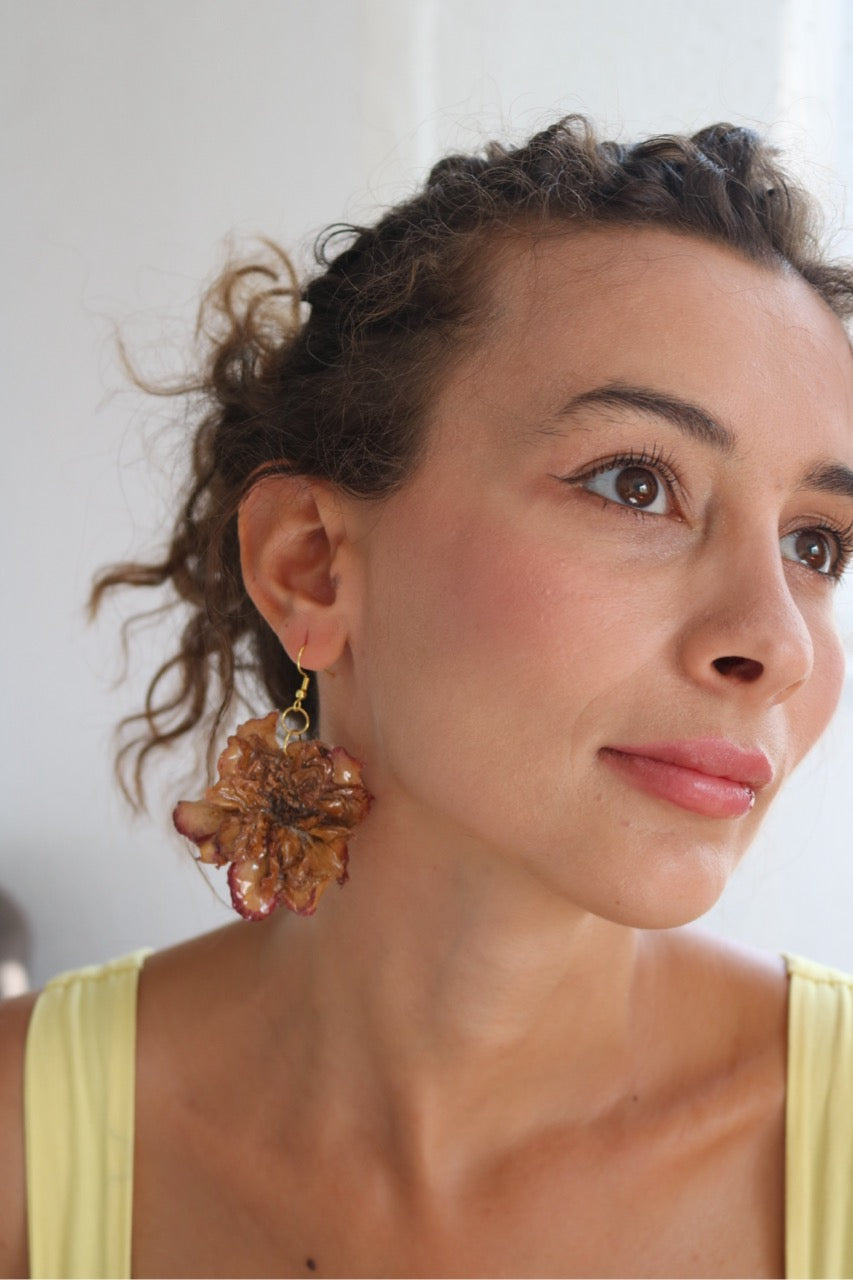 Woman wearing a pair of large, floral earrings with a neutral background